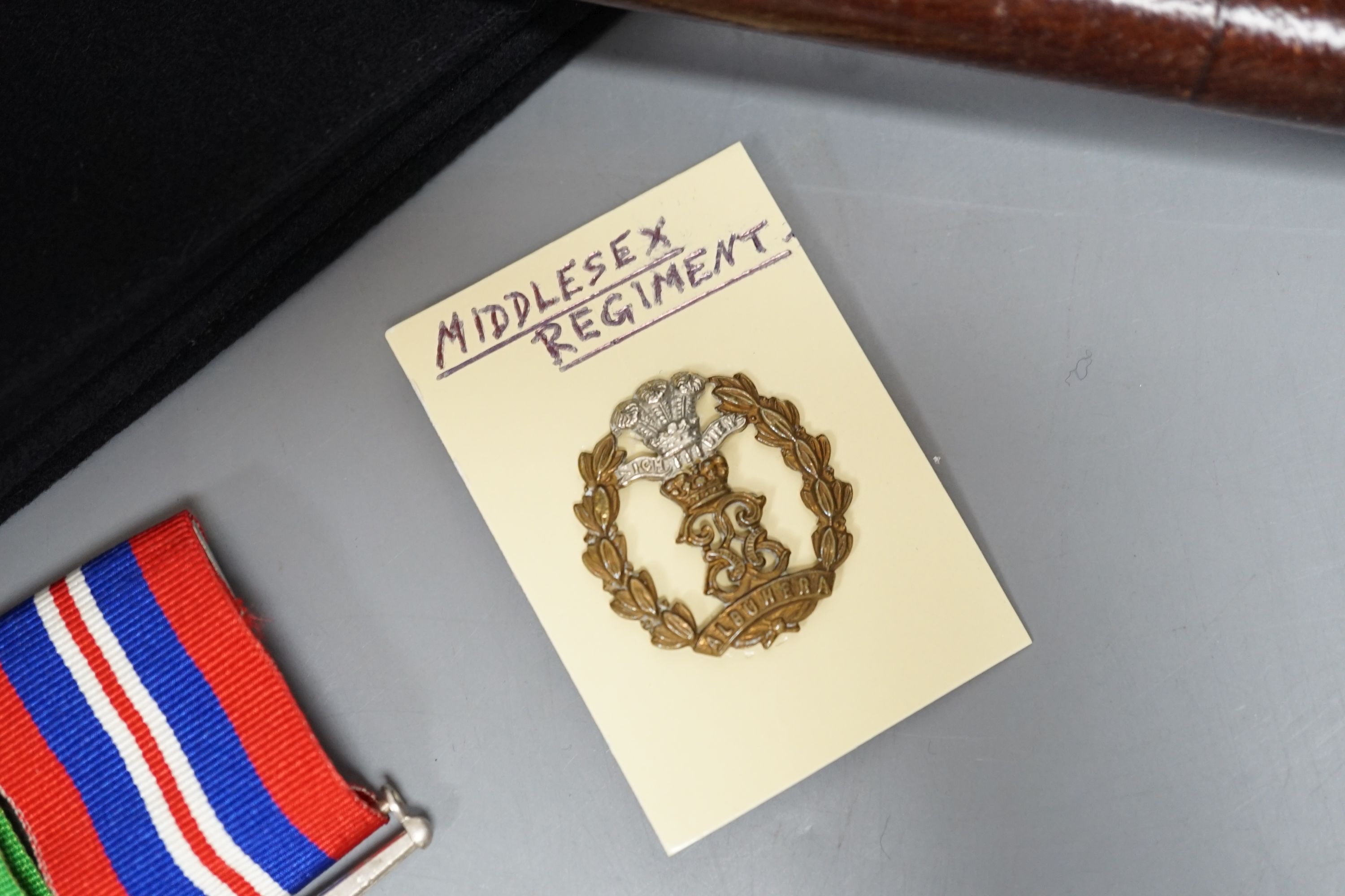 A WWII pair of medals, Middlesex Regiment cap and badge and WWI swagger stick.